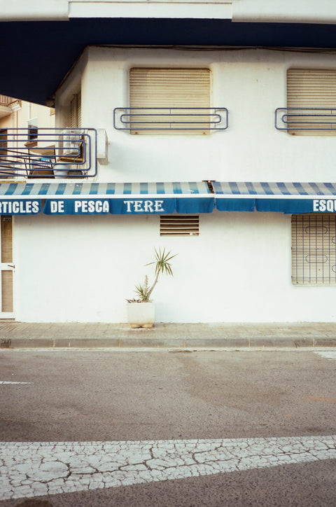 Storefront with a blue and white striped awning on a street corner.