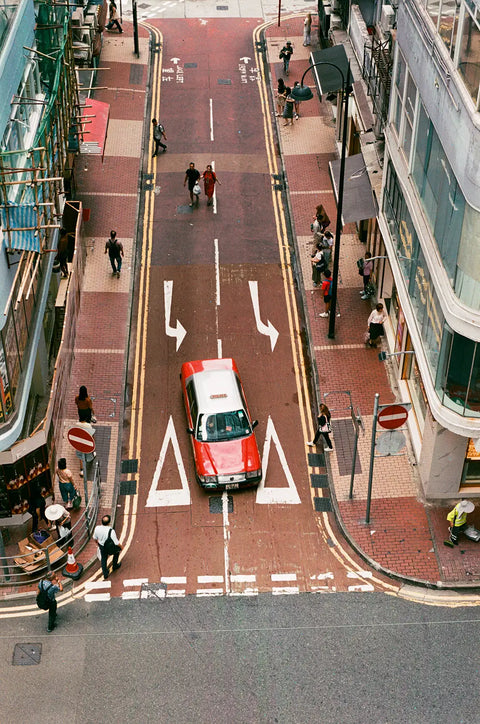 A red and white taxi on a city street with pedestrians and buildings around.