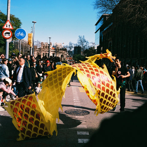 Yellow and red kite-like object on a street with people and buildings in the background