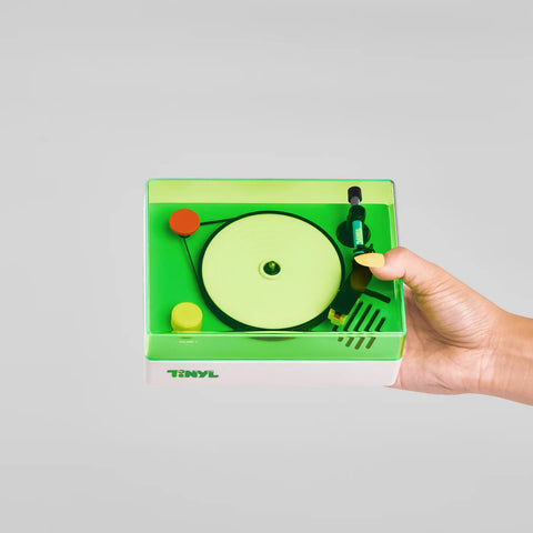 Hand holding a green cassette tape with a record player design on a gray background