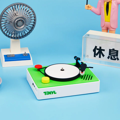 Small turntable with a record and needle on a blue background, featuring the brand 'TINYL'.