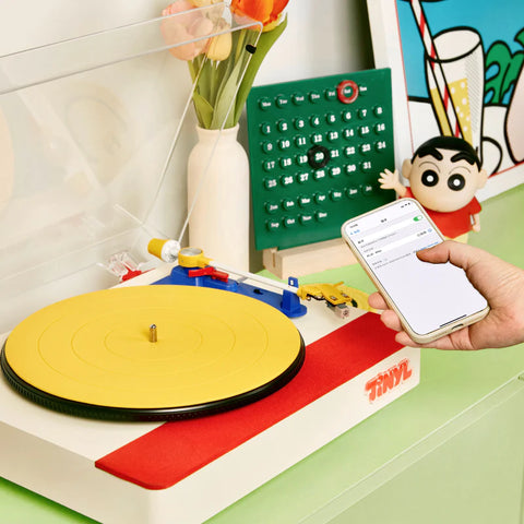 Toy record player with a hand holding a smartphone on a colorful surface.