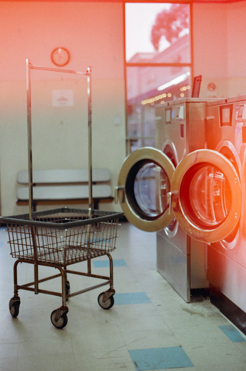 Laundry cart in front of open washing machine and dryer in a laundromat.