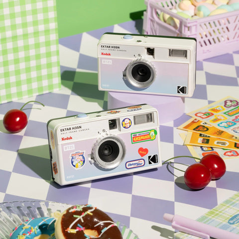 Two vintage一次性相机 on a checkered tablecloth with cookies and cherries.